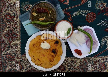 Vista laterale di makki di roti e Sarson da saag, foglie di senape curry e pane di farina di mais azzimo servito in un modo autentico stile villaggio all'aperto Foto Stock