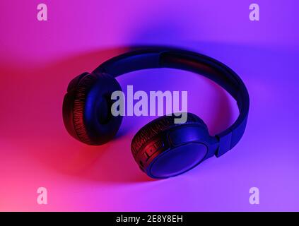 Eleganti cuffie wireless nere illuminate con coloratissima luce al neon su sfondo astratto isolato. Concetto di tecnologia moderna con spazio di copia Foto Stock