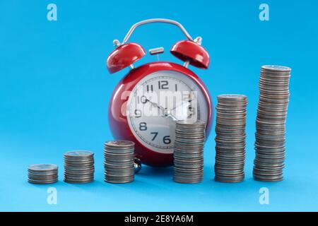Monete impilate in ordine ascendente in piedi sullo sfondo dell'allarme orologio Foto Stock