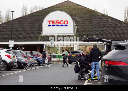 Donne su scooter elettrico mobilità fuori del supermercato Tesco superstore, gli acquirenti che indossano la maschera facciale hanno trasportato le soste nel parcheggio, Inghilterra Foto Stock