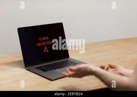 Virus rilevato su un computer portatile. Un uomo disperato che tiene le mani verso il computer con l'avviso sullo schermo. Cybercrimine, malware, un infetto Foto Stock