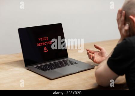 Virus rilevato su un computer portatile. Un uomo disperato seduto davanti al suo computer con l'avviso sullo schermo. Cybercrimine, infetto dispositivo non sicuro Foto Stock