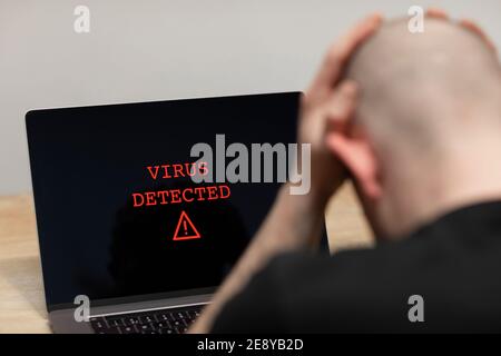 Virus rilevato con un segnale di avviso su un computer portatile. Un uomo disperato seduto davanti al suo computer con l'avviso sullo schermo. Criminalità informatica, infetta Foto Stock