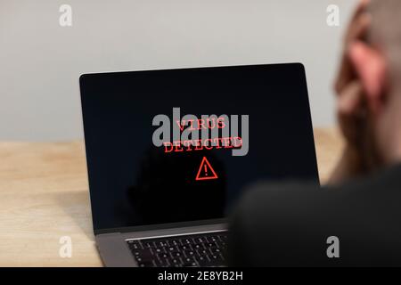 Virus rilevato con un segnale di avviso in rosso su un computer portatile. Un uomo disperato seduto davanti al suo computer con l'avviso sullo schermo. Criminalità informatica, in Foto Stock