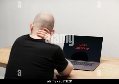 Virus rilevato con un segnale di avviso in rosso su un computer portatile. Un uomo disperato seduto davanti al suo computer con il testo sullo schermo. Criminalità informatica, infec Foto Stock