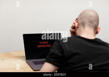 Virus rilevato e un segnale di avviso in rosso su un computer portatile. Un uomo disperato seduto di fronte al suo computer che looking al testo sul suo schermo. Criminalità informatica, Foto Stock