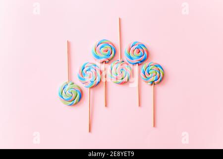 I lollipop colorati girano su bastoncini. Caramelle multicolore a spirale su sfondo rosa, vista dall'alto Foto Stock