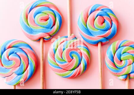 I lollipop colorati girano su bastoncini. Caramelle multicolore a spirale su sfondo rosa, vista dall'alto Foto Stock