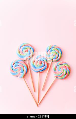 I lollipop colorati girano su bastoni di fila. Caramelle multicolore a spirale su sfondo rosa, vista dall'alto Foto Stock