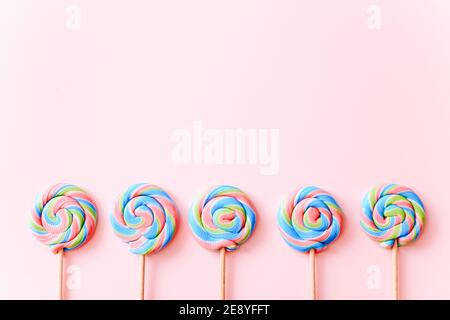 I lollipop colorati girano su bastoni di fila. Caramelle multicolore a spirale su sfondo rosa, vista dall'alto Foto Stock