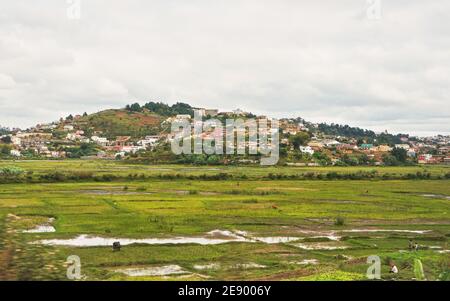 Antananarivo, Madagascar - 24 aprile 2019: Paesaggi tipici durante la giornata di overcast vicino alla capitale del Madagascar, case su piccole colline sullo sfondo, con la gente Foto Stock