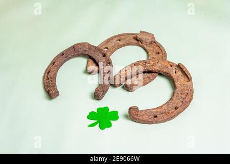 Ferro di cavallo gravemente usurato con una foglia di trifoglio in feltro. Simbolo di buona fortuna, concetto di giorno di San Patrizio. Sfondo in vinile verde chiaro Foto Stock