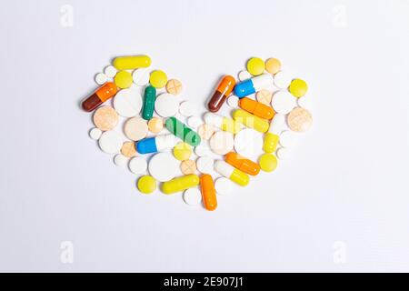 Pillole, compresse e capsule di medicina farmaceutica assortite per il trattamento delle malattie cardiache isolate su sfondo bianco. Forma del cuore, spazio di copia Foto Stock