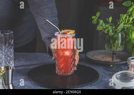 Donna ha messo sul tavolo highball vetro di pompelmo rosa Mezcal Paloma cocktail in casa reale. Nuovo concetto di vita della quarantena. Profondità superficiale del fuoco Foto Stock