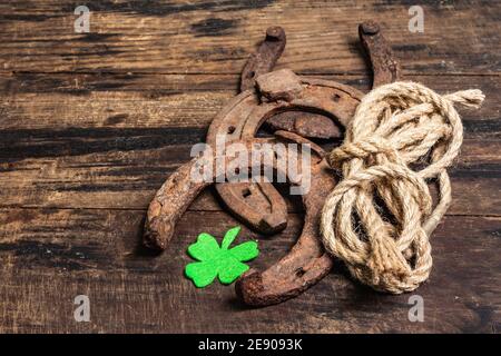 Ferro di cavallo, corda e foglia di trifoglio in feltro mal indossati. Simbolo di buona fortuna, concetto di giorno di San Patrizio. Vintage tavole di legno sfondo Foto Stock