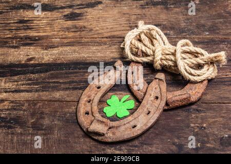 Ferro di cavallo, corda e foglia di trifoglio in feltro mal indossati. Simbolo di buona fortuna, concetto di giorno di San Patrizio. Vintage tavole di legno sfondo Foto Stock