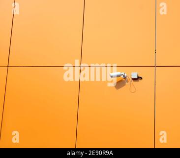 Telecamera di sicurezza montata sulla parete dell'edificio moderno rifinita in arancione primo piano della vista orizzontale dei pannelli Foto Stock