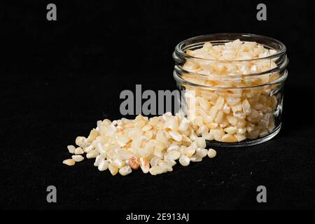 Semi di mais bianchi rotti in un vaso di vetro su una superficie nera. Foto Stock