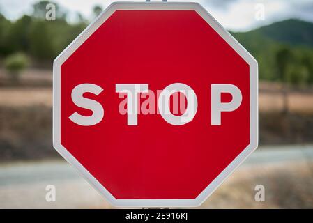 dettaglio di un segnale di stop ottagonale con sfondo rosso un cielo blu e alcuni alberi su un'autostrada Foto Stock