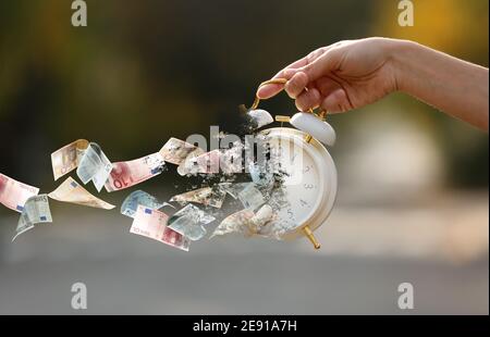 Donna che tiene la sveglia sbriciolare con le banconote in euro volanti all'aperto Foto Stock