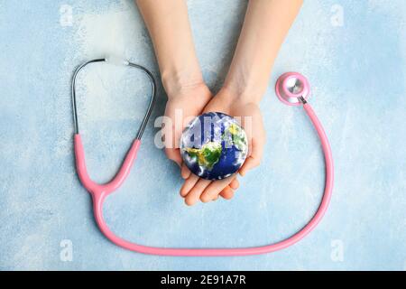Mani femminili con stetoscopio e modello di Terra su sfondo a colori. Concetto di ecologia Foto Stock
