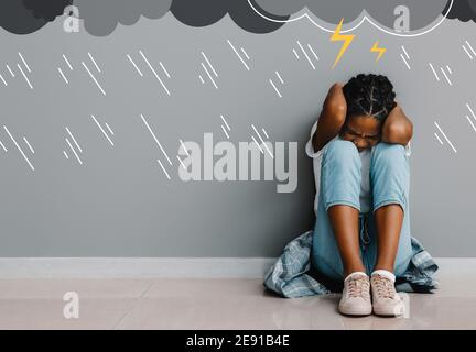 Stressata afroamericana ragazza seduta vicino parete grigia Foto Stock