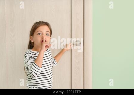 Carina bambina che mostra il gesto del silenzio vicino alla porta chiusa Foto Stock