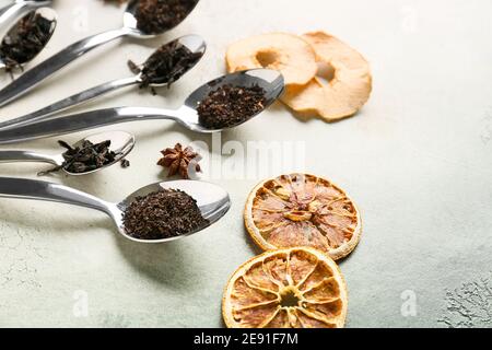 Cucchiai con foglie secche di tè nero e frutta secca sfondo chiaro Foto Stock