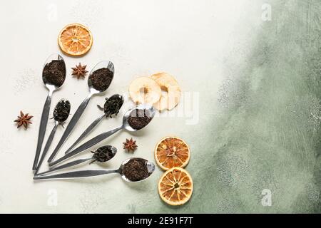 Cucchiai con foglie secche di tè nero e frutta secca sfondo chiaro Foto Stock