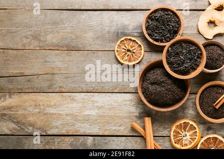 Ciotole con foglie secche di tè nero, spezie e frutta secca su sfondo di legno Foto Stock