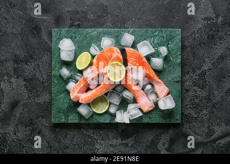 Bistecche di salmone crudo, cubetti di limone e ghiaccio su sfondo scuro Foto Stock