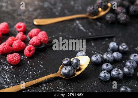 Cucchiai con bacche diverse su sfondo scuro Foto Stock