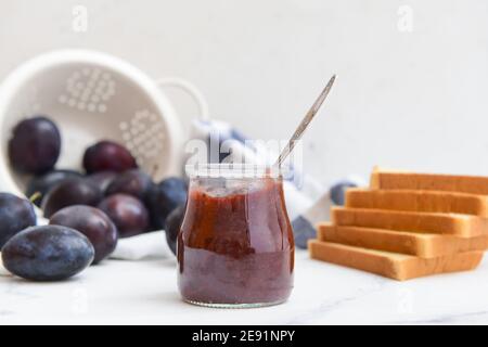 Vaso in vetro con deliziosa marmellata di prugne fatta in casa su sfondo chiaro Foto Stock