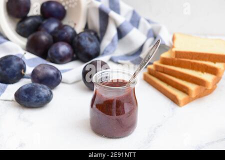 Vaso in vetro con deliziosa marmellata di prugne fatta in casa su sfondo chiaro Foto Stock