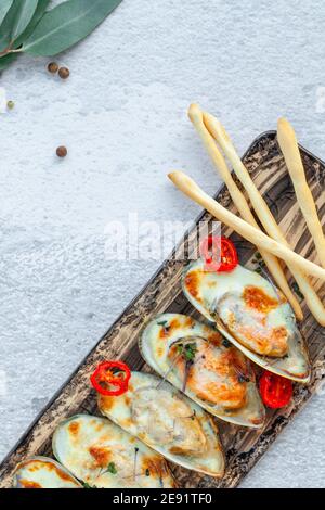 Porzione di cozze cotte al forno con parmigiano su piatto rettangolare Foto Stock