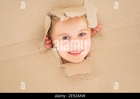 Allegra bambina che guarda dal foro in scatola di cartone. Foto Stock