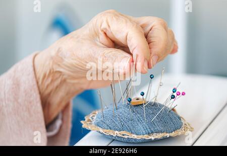Mano pulita di donna anziana che prende l'ago dal cuscino Foto Stock