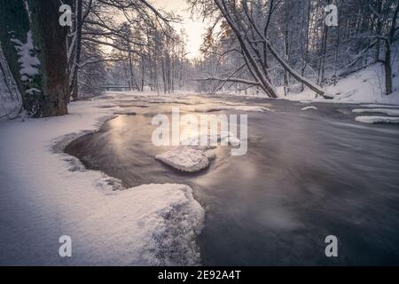 Scenic inverno paesaggio con fiume che scorre e la luce del mattino in Finlandia. Alberi innevati. Foto Stock