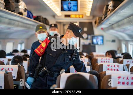 (210202) -- URUMQI, 2 febbraio 2021 (Xinhua) -- Zhang Jianzhi parla con i passeggeri mentre effettua il controllo di sicurezza sul treno D8806 nella regione autonoma Xinjiang Uygur della Cina nord-occidentale, 30 gennaio 2021. Zhang Jianzhi, un poliziotto ferroviario di 27 anni che lavora a Urumqi, si fa occupato del suo terzo lavoro di corsa del Festival di primavera. Lavorando per più di 40 giorni consecutivi durante la corsa di viaggio del Festival di Primavera dello scorso anno, Zhang si è sentito dispiaciuto per non essere stato con la sua fidanzata Zhao Lelin. Quest'anno, infine, ha proposto alla sua ragazza sul suo noto treno D8806. "Ho programmato questa proposta speciale sul treno per Foto Stock