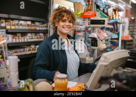 Ritratto di una donna felice che lavora al banco cassa sorridendo alla macchina fotografica. I dipendenti del supermercato lavorano al banco del registratore di cassa. Foto Stock