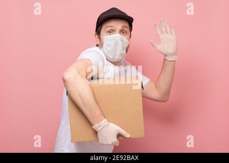 Addetto alla consegna che tiene una scatola di cartone in guanti e maschera di gomma per uso medico. Acquisti online e consegna espressa in quarantena Foto Stock