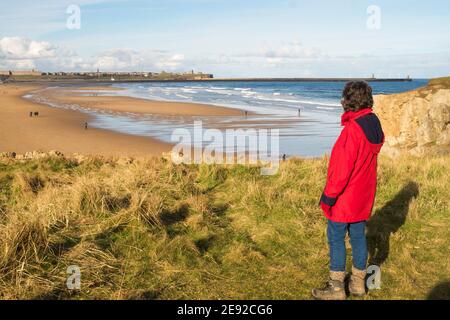 Vista posteriore di una donna che guarda sulla spiaggia di Sandhaven verso Tynemouth, a South Shields, Inghilterra nord-orientale, Regno Unito Foto Stock