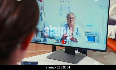 Vista posteriore di un infermiere che discute su webcam con uno specialista senior stomatologo utilizzando il telefono cellulare seduto in clinica dentale di fronte al pc con radiografia digitale. Medico di odontoiatria che spiega i sintomi del paziente Foto Stock