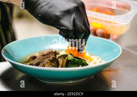 Chef che prepara zuppa di noodle ramen con carne, uova e verdure in un ristorante Foto Stock