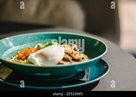 Zuppa di ramen di manzo con uova in camicia e verdure a un ristorante Foto Stock