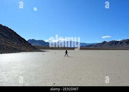 Donna che cammina sull'ippodromo Playa in un freddo giorno di dicembre nel Death Valley National Park, bellissimo paesaggio con le rocce in movimento che lasciano tracce Foto Stock