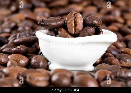 Primo piano di una piccola vasca da bagno bianca piena di chicchi di caffè circondati da chicchi tostati sparsi. Concetto di potenza rinfrescante per il caffè. Scatto in studio, selezione f Foto Stock