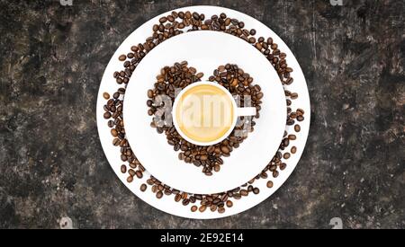 Simbolo del cuore composto da chicchi di caffè con una tazza di caffè su un tavolo scuro e grugnoso Foto Stock