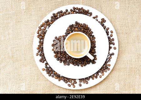 Simbolo del cuore fatto di chicchi di caffè torrefatti e porcellana tazza di caffè espresso sullo sfondo di un panno Foto Stock