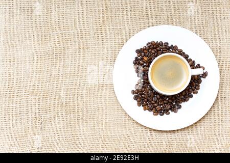 Simbolo del cuore composto da chicchi di caffè tostati e un caffè cuocetella su uno sfondo di tela di tela Foto Stock